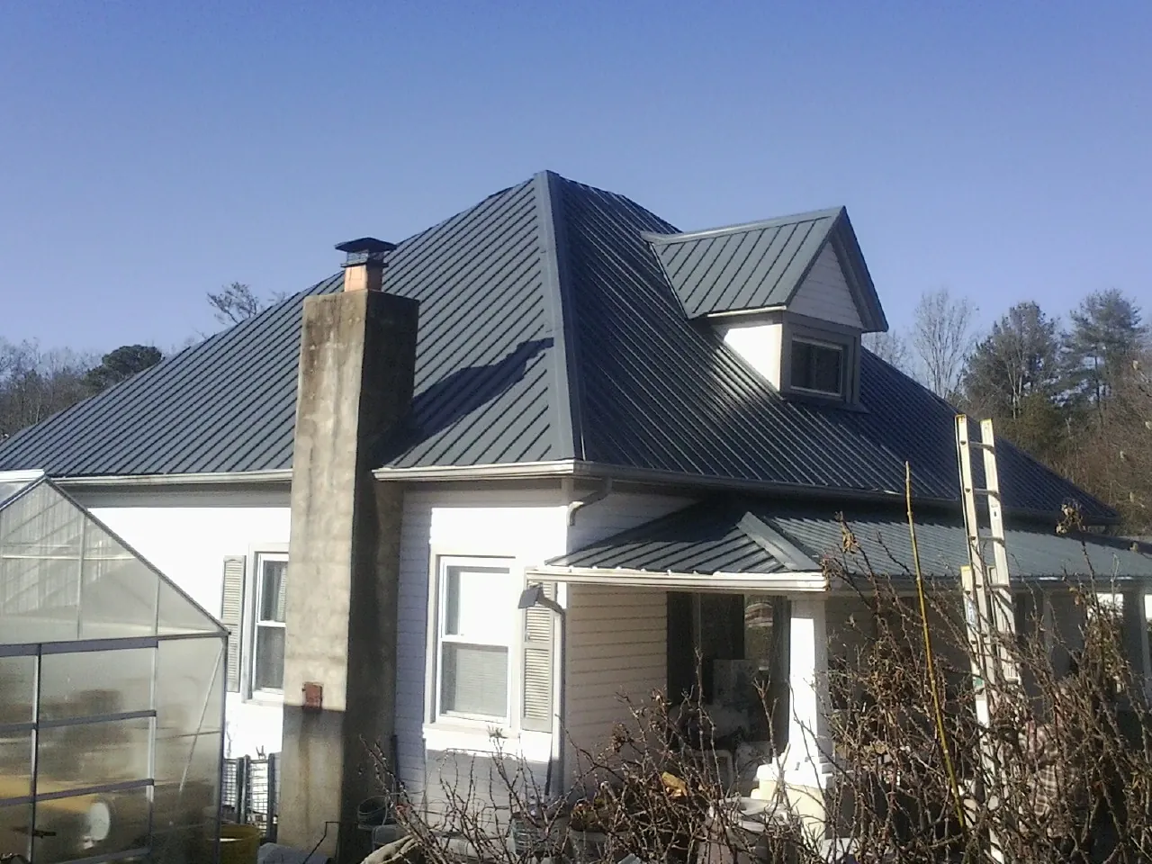 Dark blue standing seam metal roof on a white farmhouse with dormer — Slate & Tile Roof Repair by Roofing Brothers in Wynne