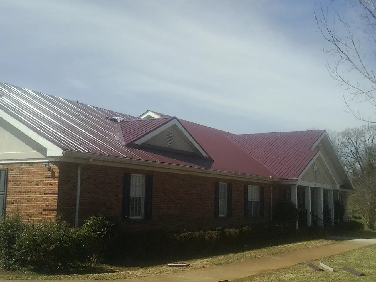 Red metal roof with gabled entries on a long brick building, from a Hail Damage Roof Repair job in Wynne