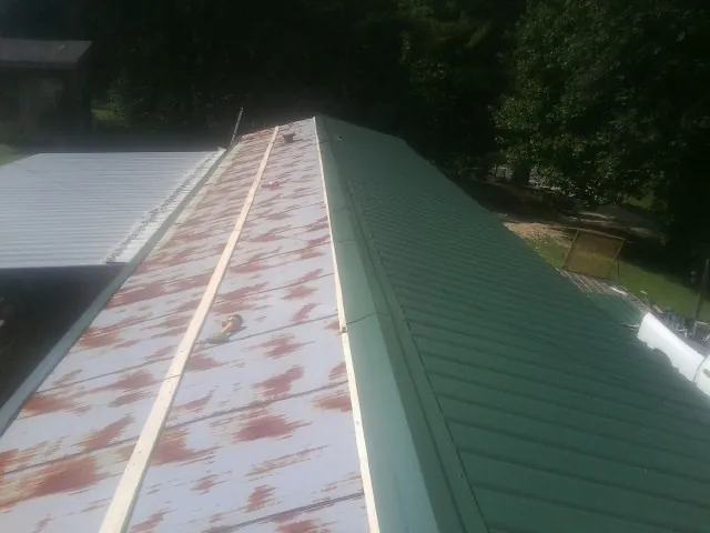 Old rusted panels beside newly installed green metal roofing — Wind Damage Roof Repair by Roofing Brothers in Wynne