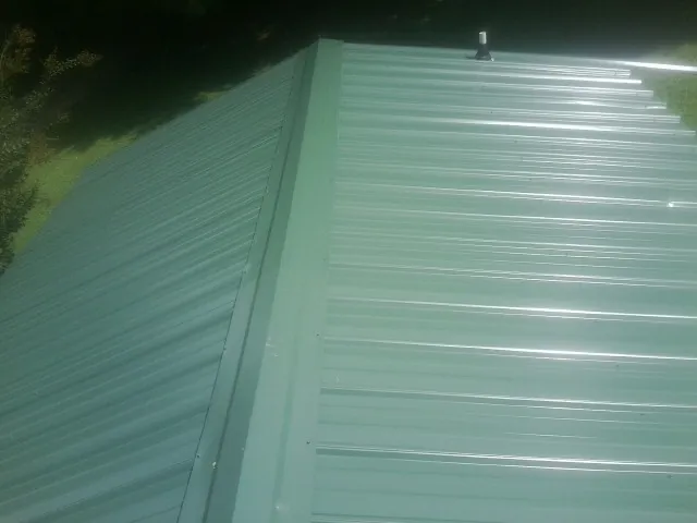 New green metal panels meeting at the ridge of a roof — Flat Roof Repair work by our crew in Wynne