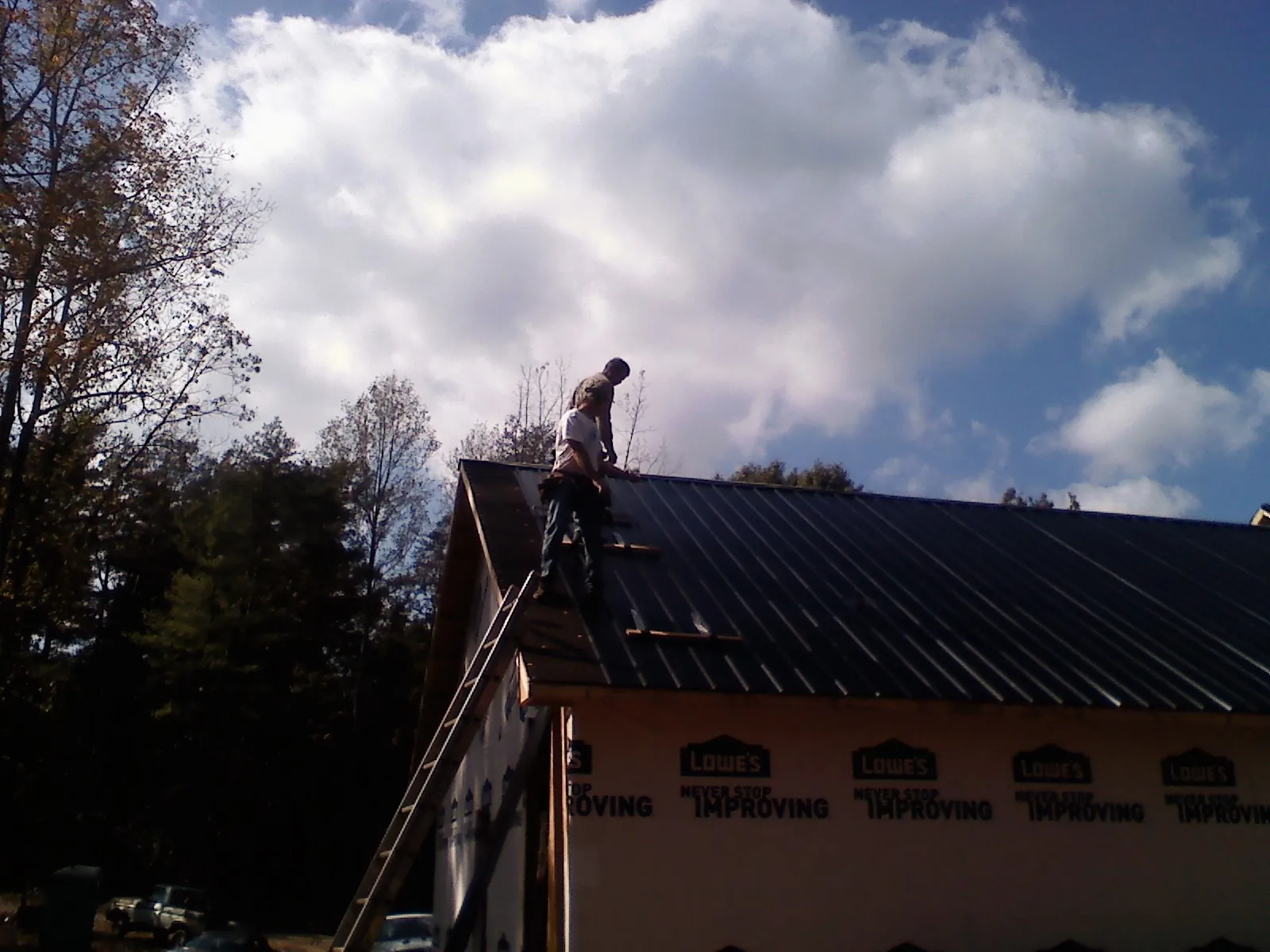 Roofer fastening dark metal panels high against a cloudy sky, from a Roof Inspection job in Wynne