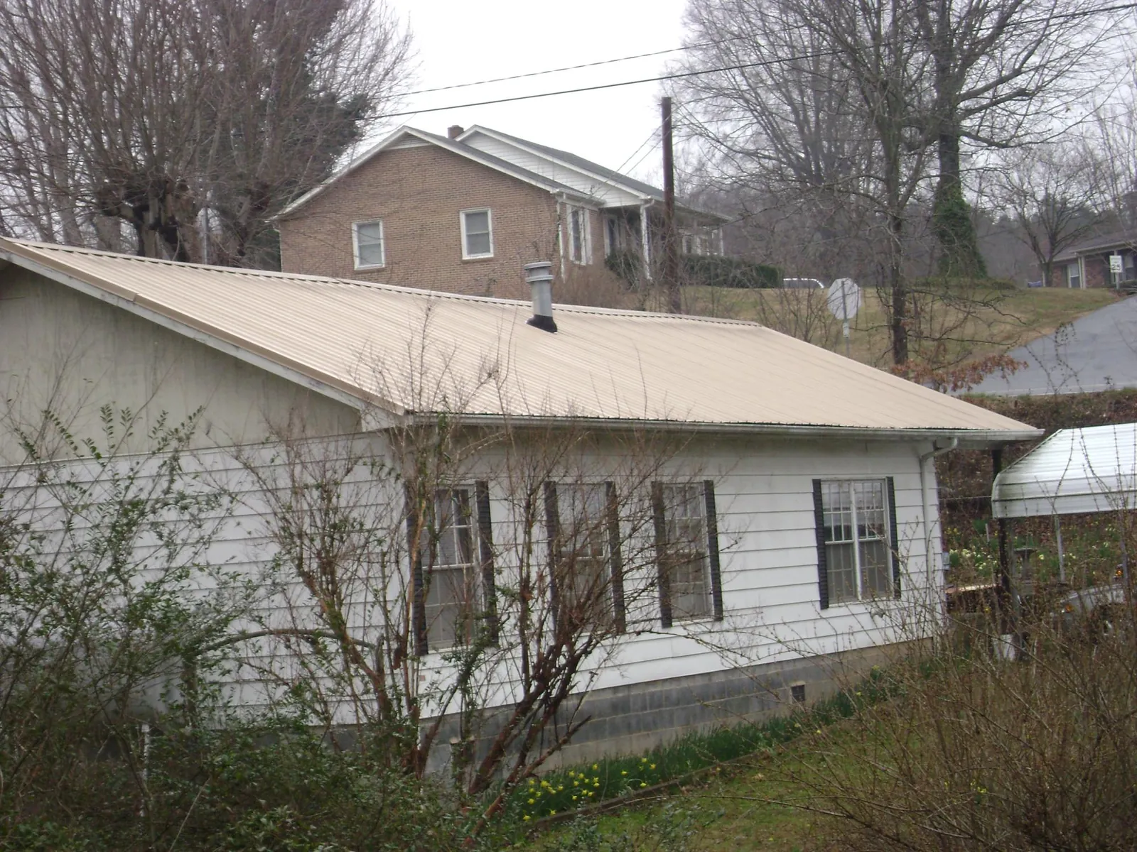 Tan metal roof on a white sided house set into a hillside — Commercial Roofing by Roofing Brothers in Wynne