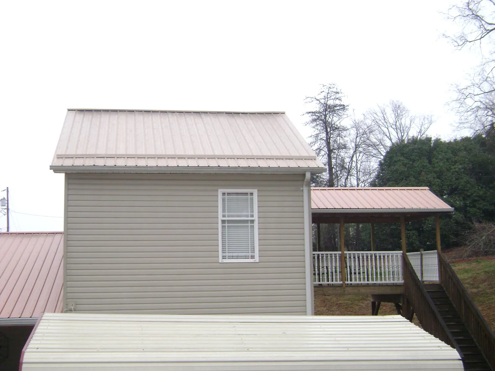 Tan metal roofs on a two story addition and attached porch, from a Roof Replacement job in Wynne