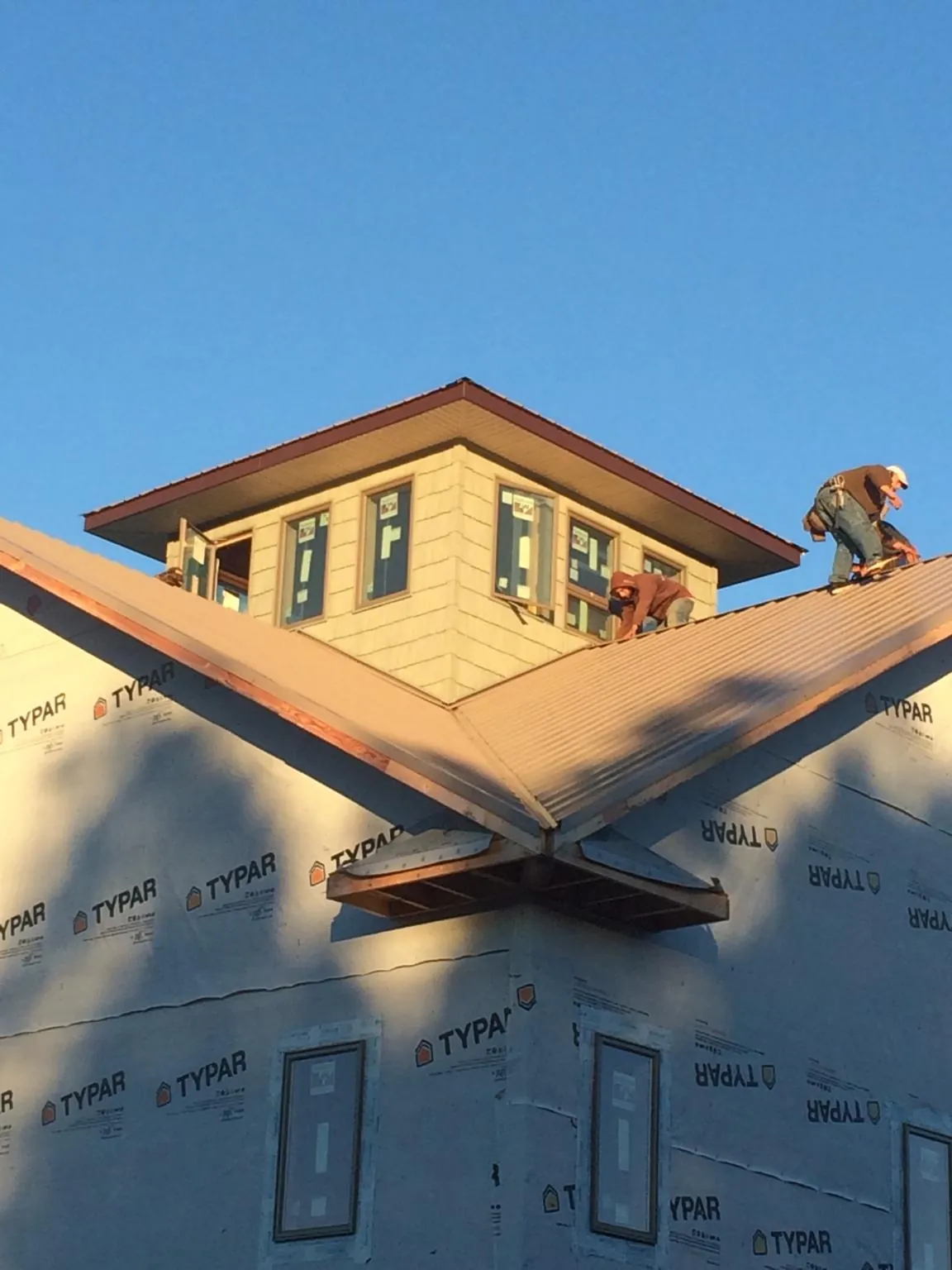 Roofers working around a rooftop cupola on a new metal roof at sunset — Roof Waterproofing in Wynne by Roofing Brothers